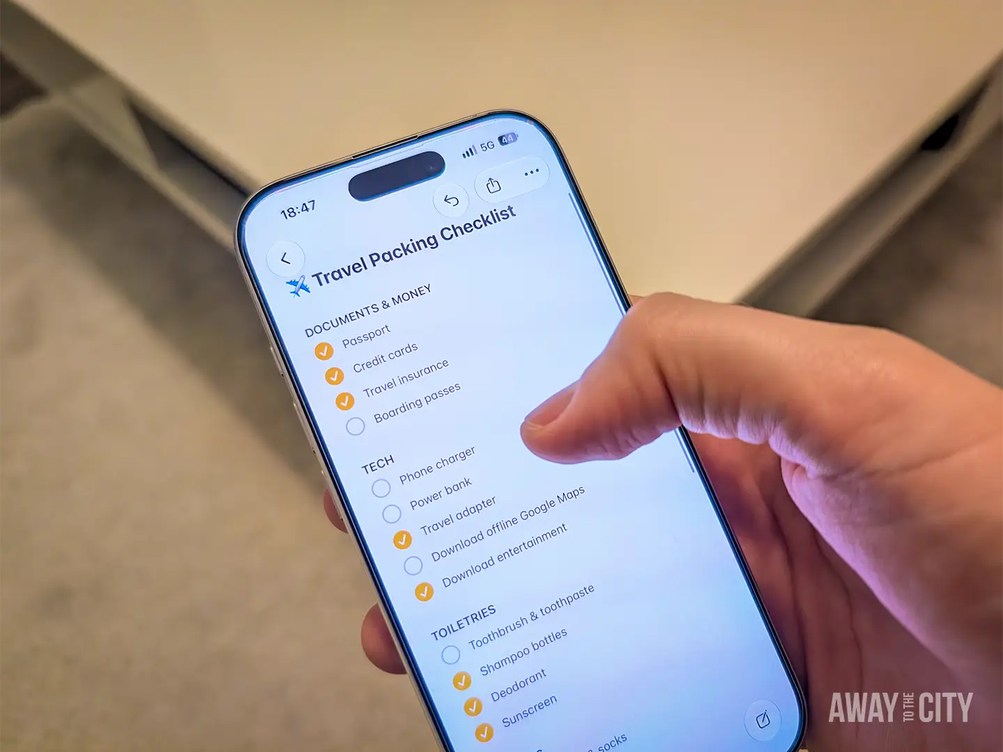 Hand holding a smartphone displaying a Travel Packing Checklist with tick boxes for different categories, which is one of the best travel packing hacks so you never forget any items.