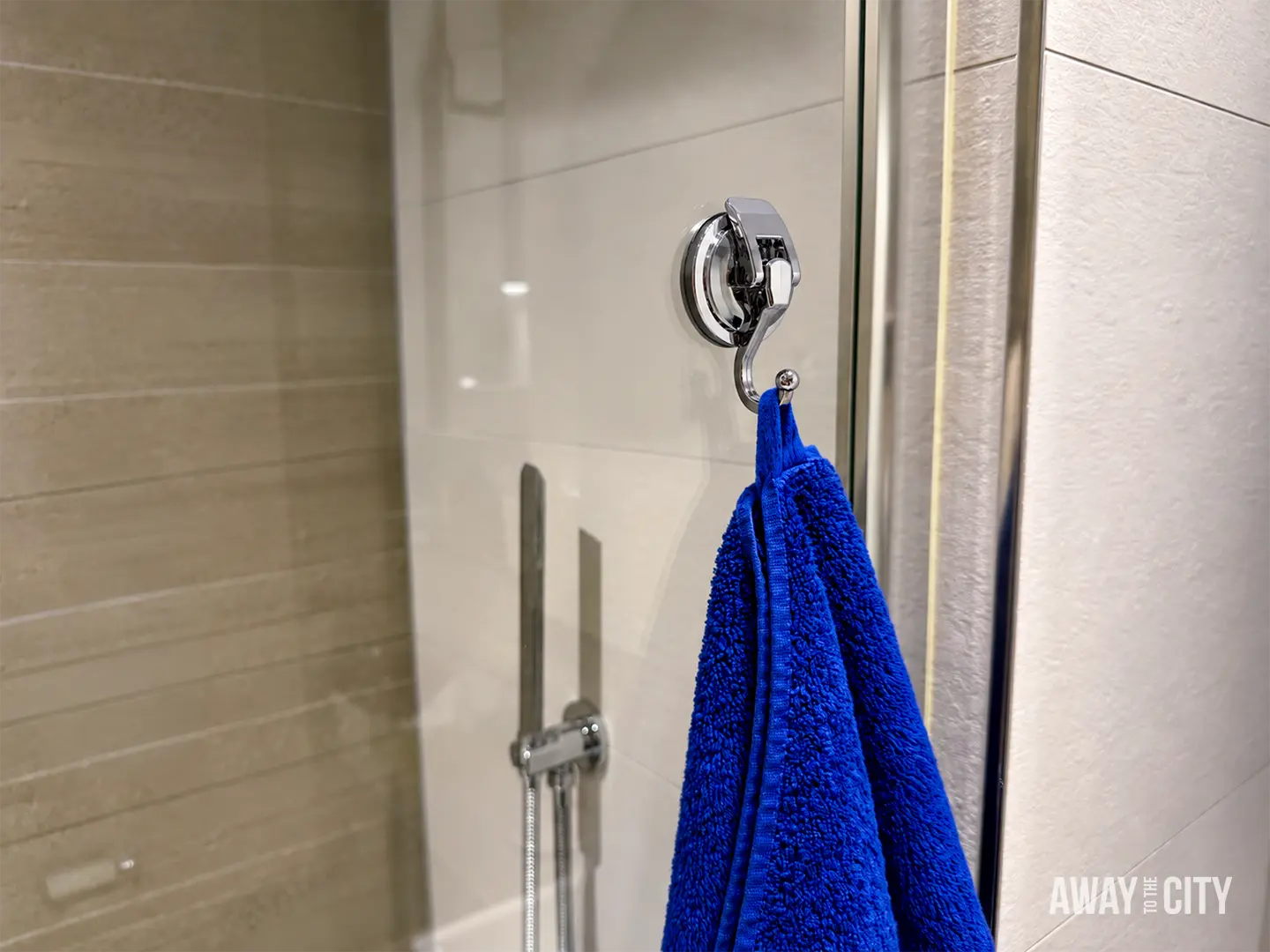 Blue towel hanging from a suction hook attached to a glass shower door, demonstrating a space-saving travel accessory.