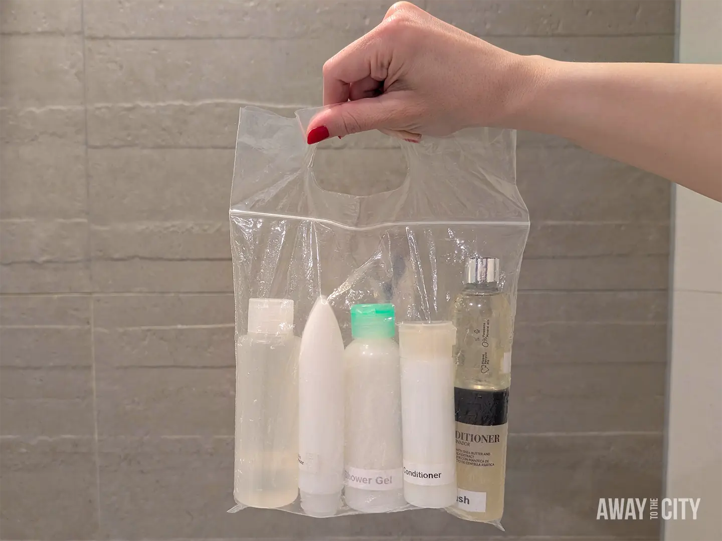Hand holding a clear resealable liquids bag containing travel-sized toiletries, including shampoo, conditioner and skincare products.