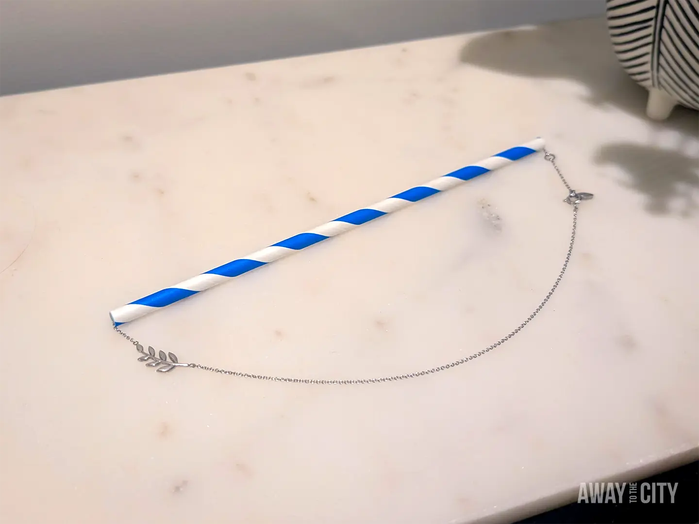 Silver necklace threaded through a drinking straw to prevent tangling when packing jewellery for travel, which is a cheap packing tip for a trip.