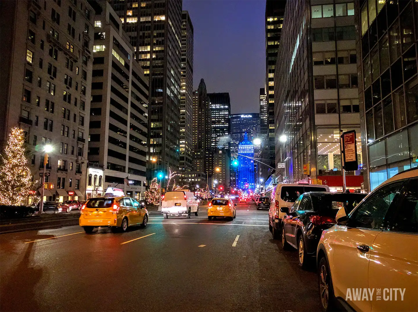 Night street scene along Park Avenue in Midtown Manhattan, New York, with yellow taxis, illuminated skyscrapers and Christmas decorations lining the busy avenue.