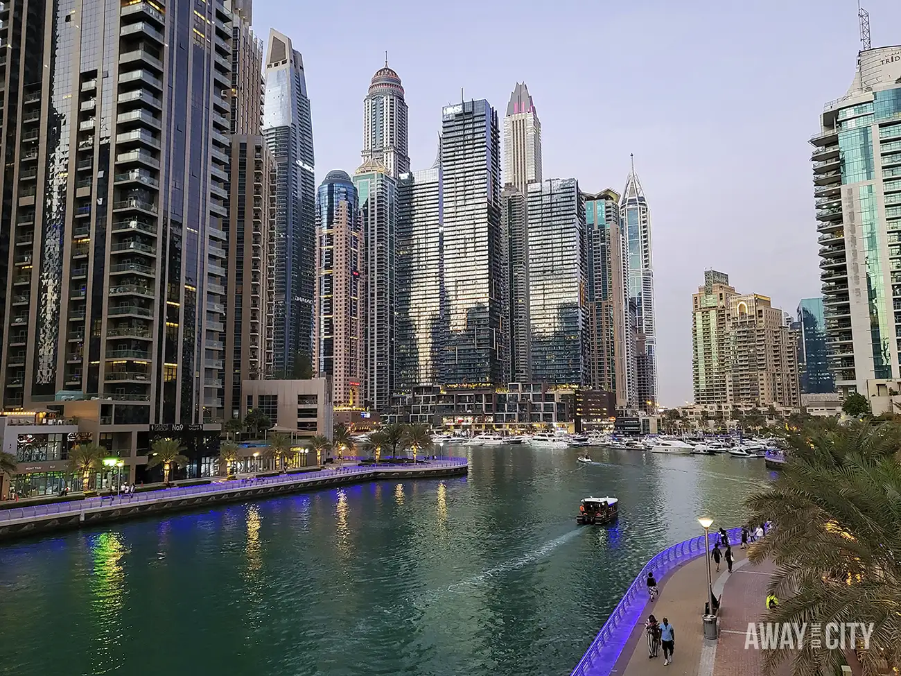 Dubai Marina skyline at dusk with glass skyscrapers, canal, yachts and lit promenade.