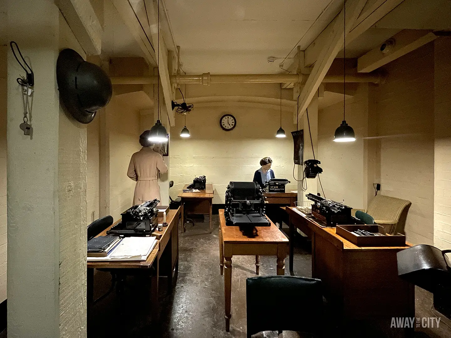 A historical wartime office with two mannequins dressed in period clothing and working on typewriters.