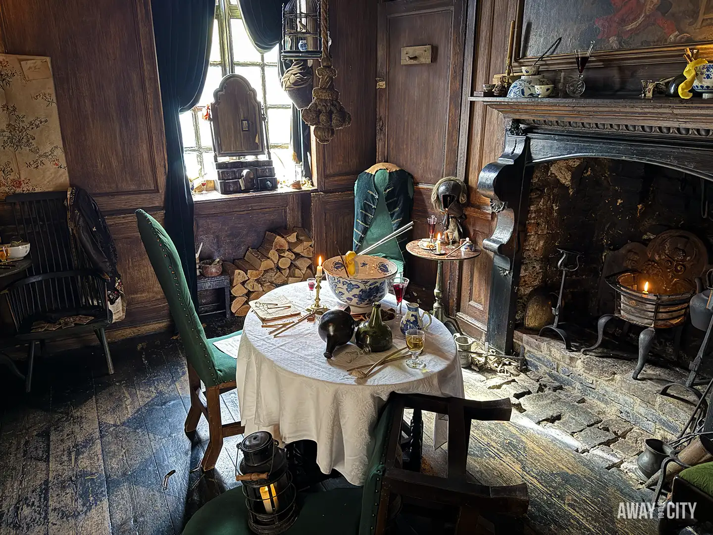 A darkly-lit, historic interior of Dennis Severs' House in London, set up as if the occupants just left the table beside a sooty fireplace.