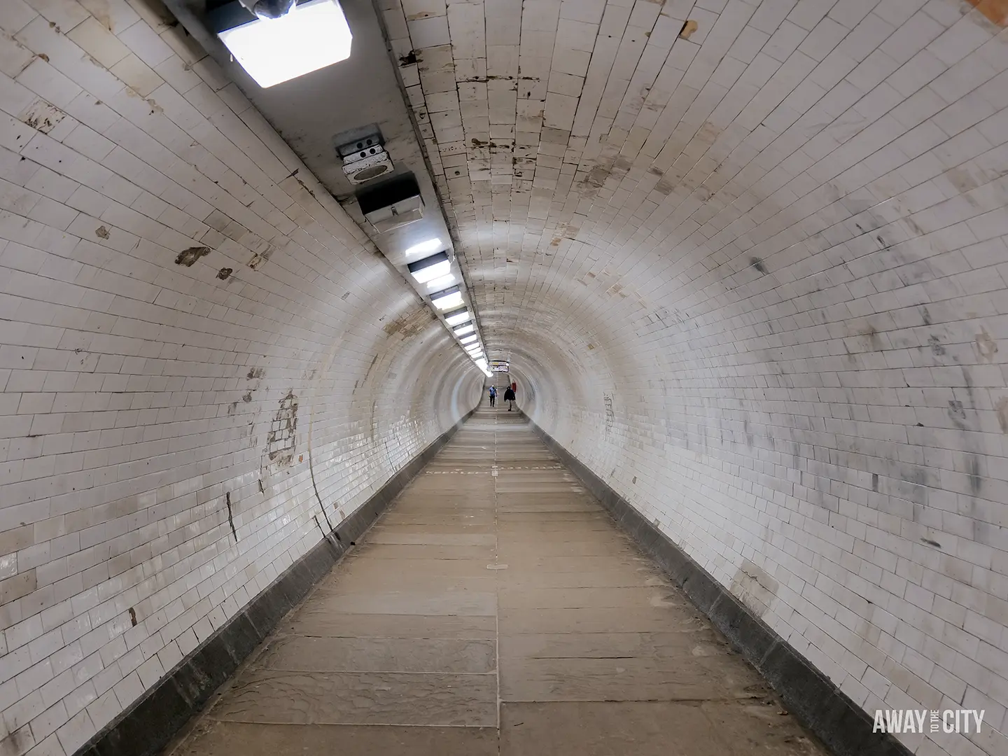 The long, tiled Greenwich foot tunnel stretches into the distance, with a few people walking towards the end.