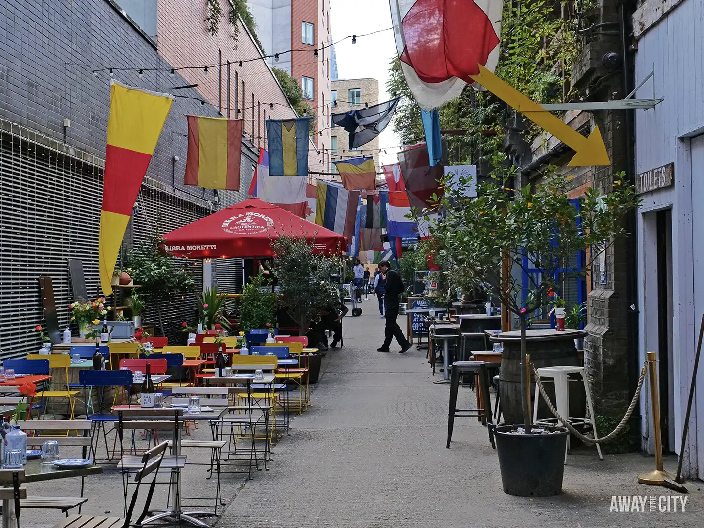 A deserted Maltby Street Market alleyway with colourful flags and empty tables and chairs.