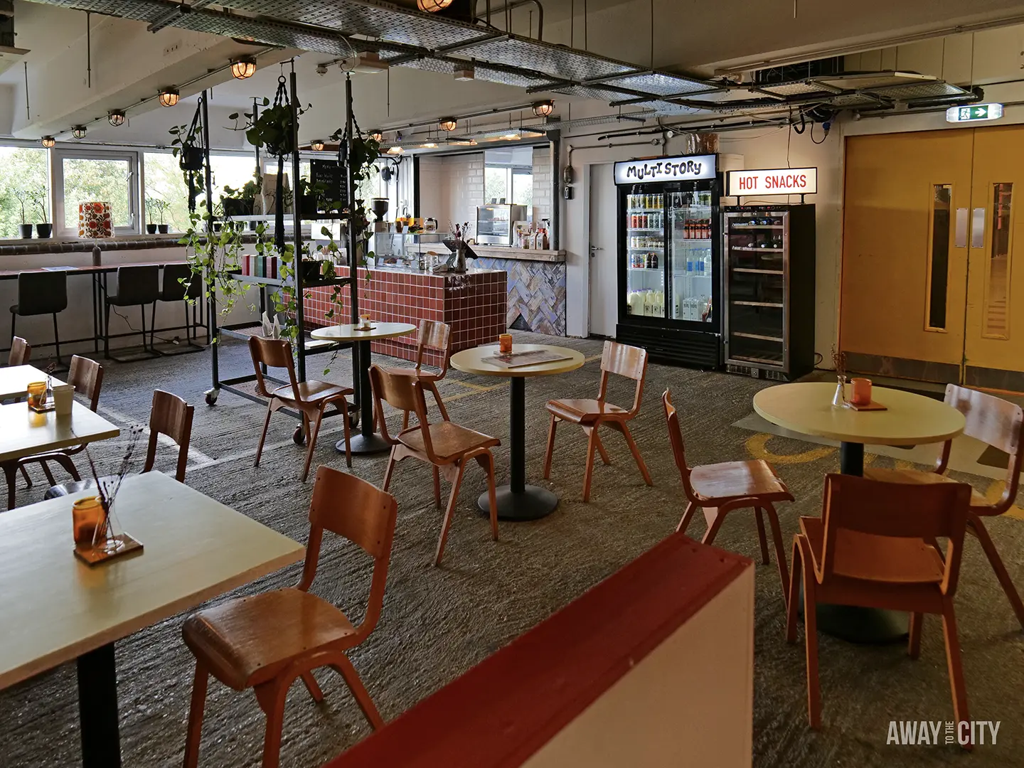 A brightly lit, spacious cafe within the Peckham Levels complex, with a variety of wooden tables and chairs, a counter, and large windows.