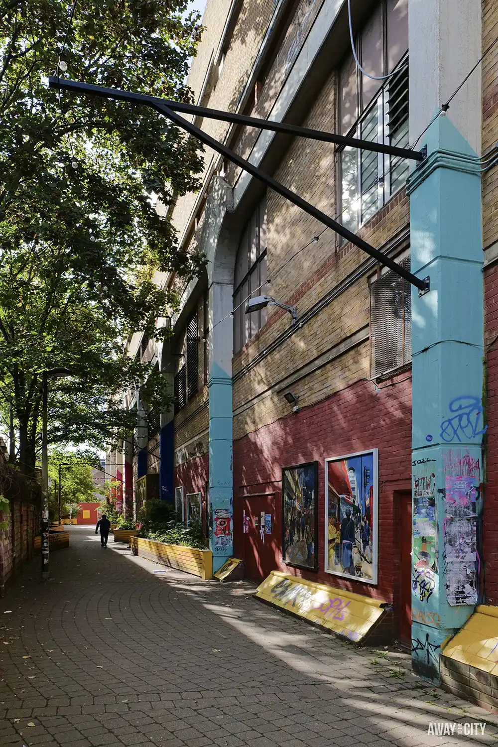 A pedestrian walkway alongside the brick exterior of Peckham Levels, with colourful pillars and artwork on the walls.