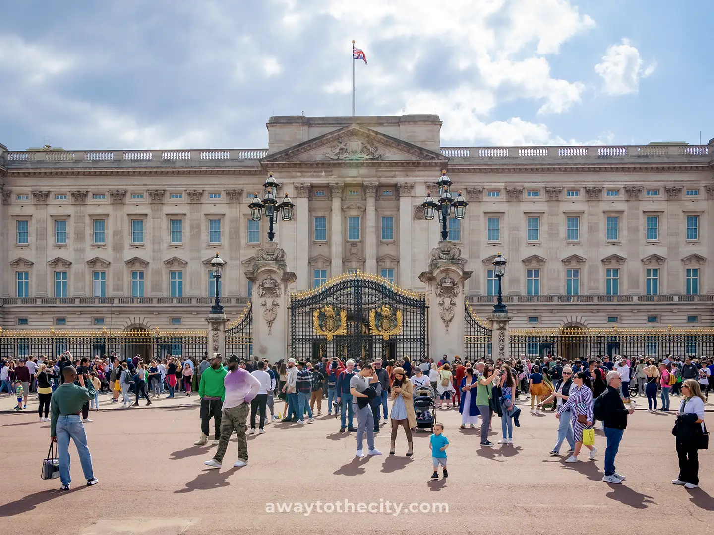 Buckingham Palace's grand facade is visible, with many tourists gathered in front of its golden gates.