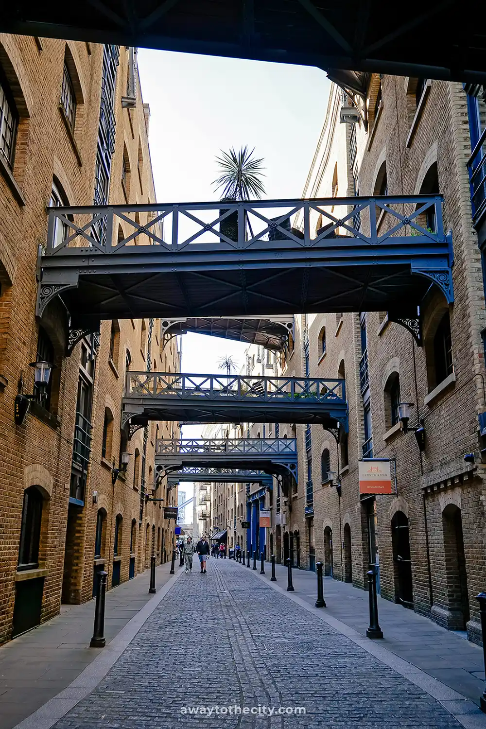 A historic cobbled street in Butler's Wharf, Shad Thames, features overhead walkways connecting old brick warehouses.