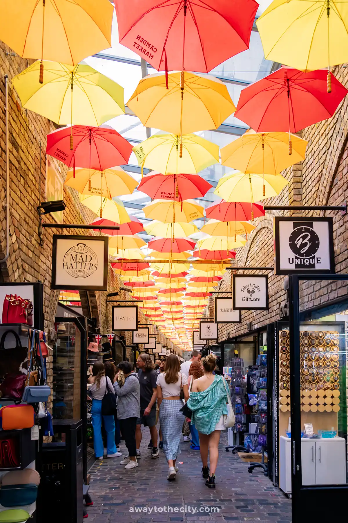 A busy market street in Camden is covered by a canopy of red and yellow umbrellas, one of the best things to see in London.