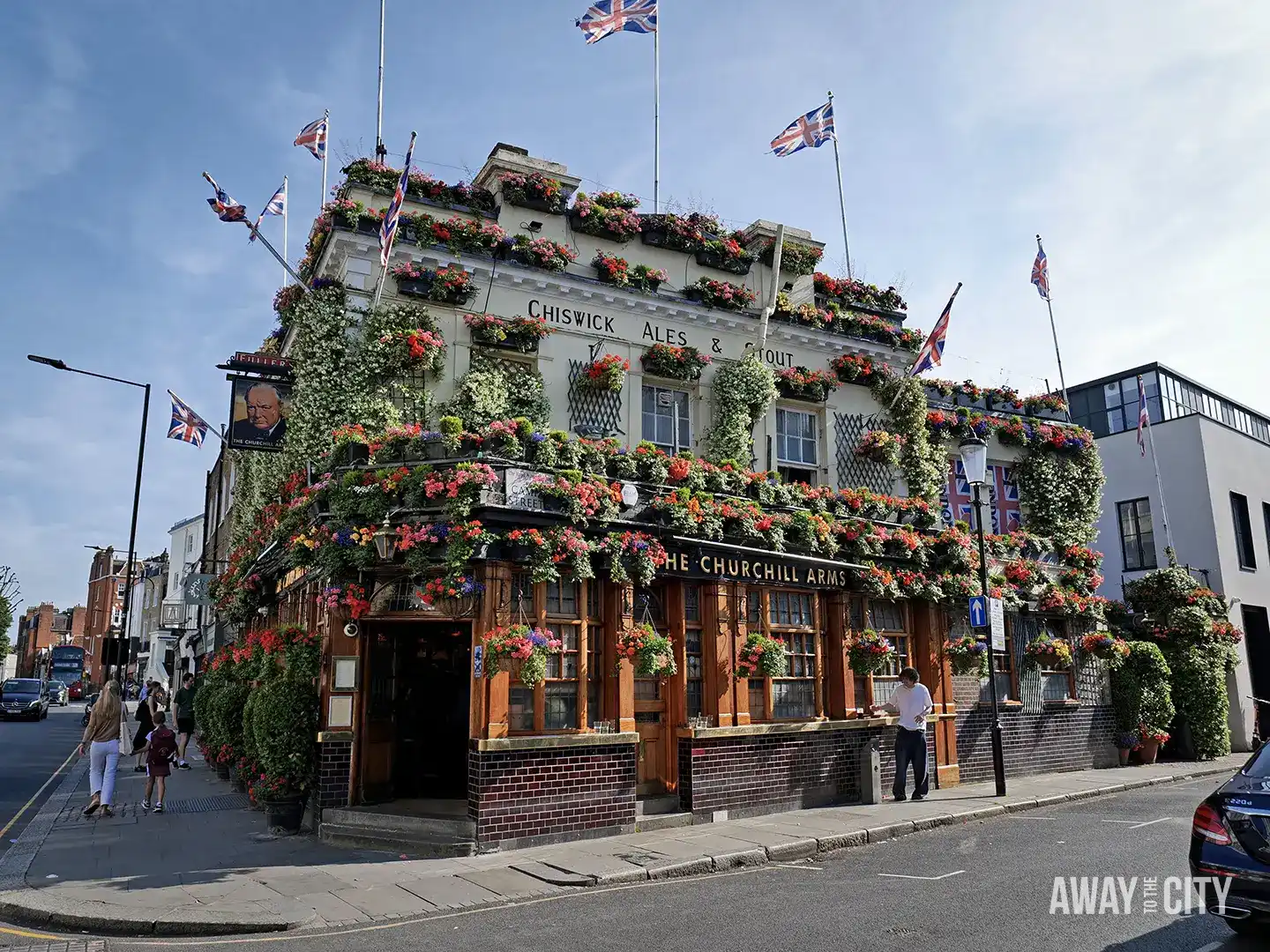 The Churchill Arms pub in London is covered in a dense display of flowers and greenery, with several Union Jack flags flying from the rooftop.