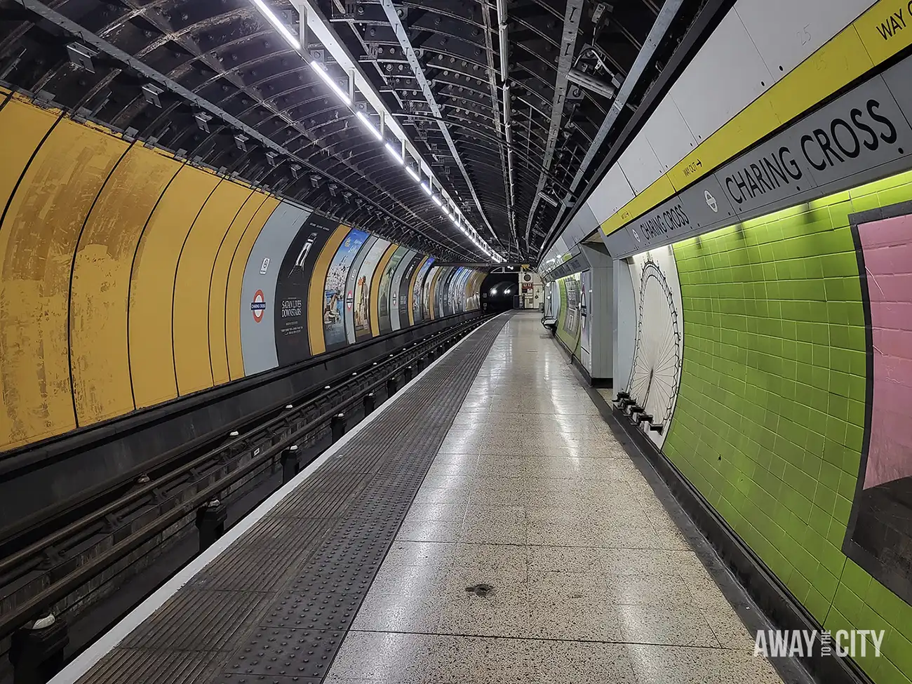 An abandoned London Underground station platform at Charing Cross, with colourful advertising boards and a sign for Charing Cross visible on the wall.