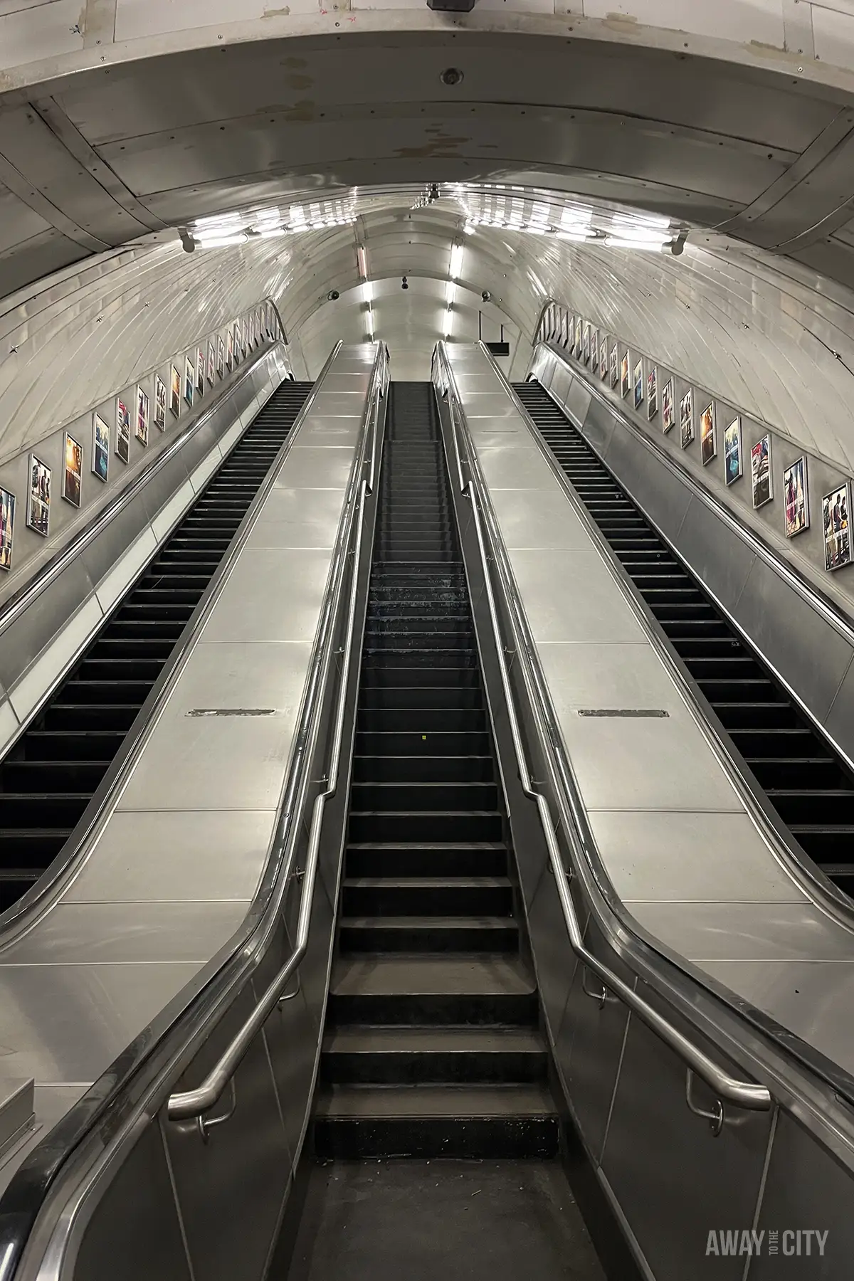 Three sets of escalators lead into a bright, white, vaulted tunnel decorated with small pictures along the walls.