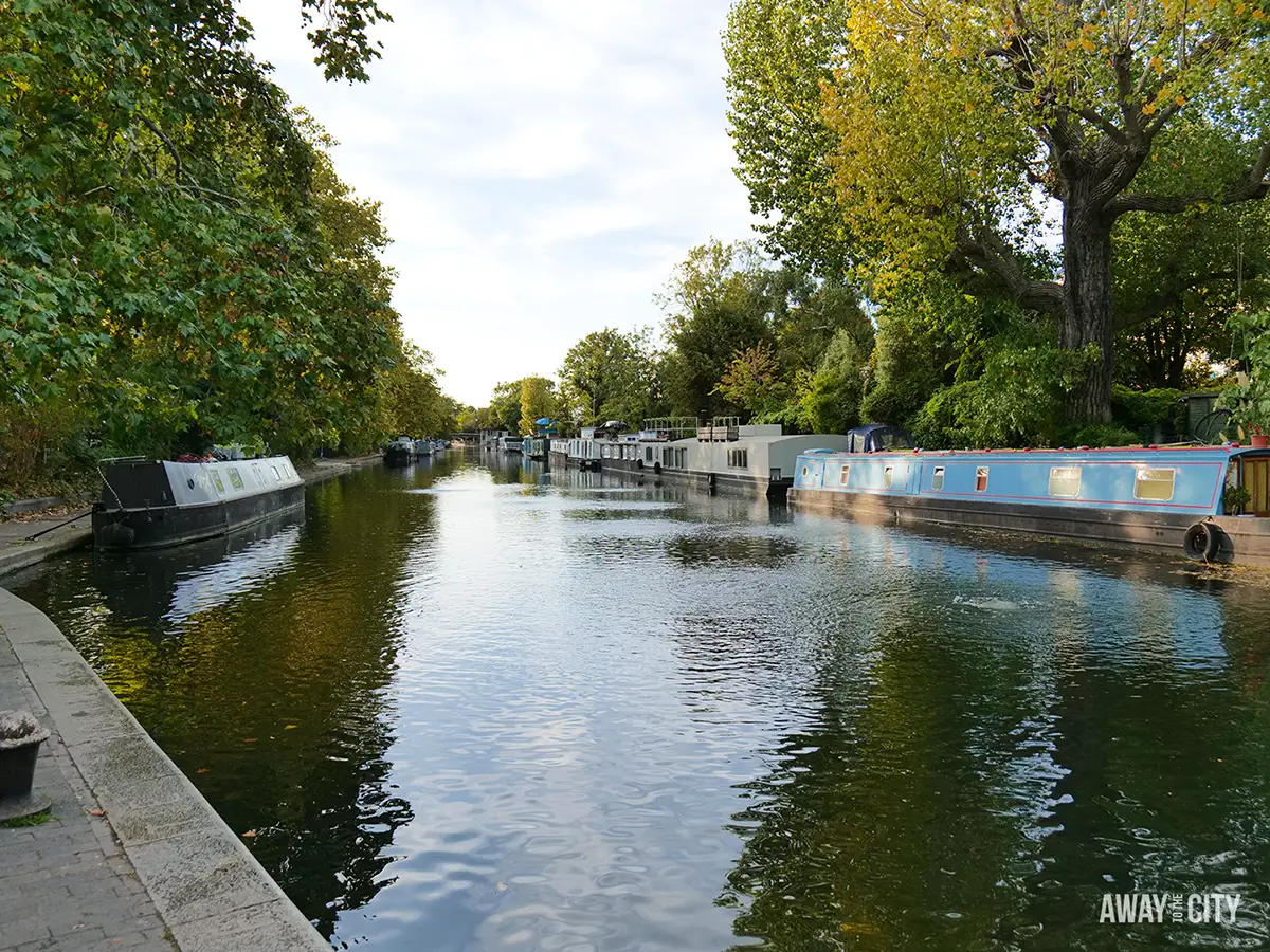Colourful houseboats moored along the tranquil canal in Little Venice, London, lined with green autumnal trees.
