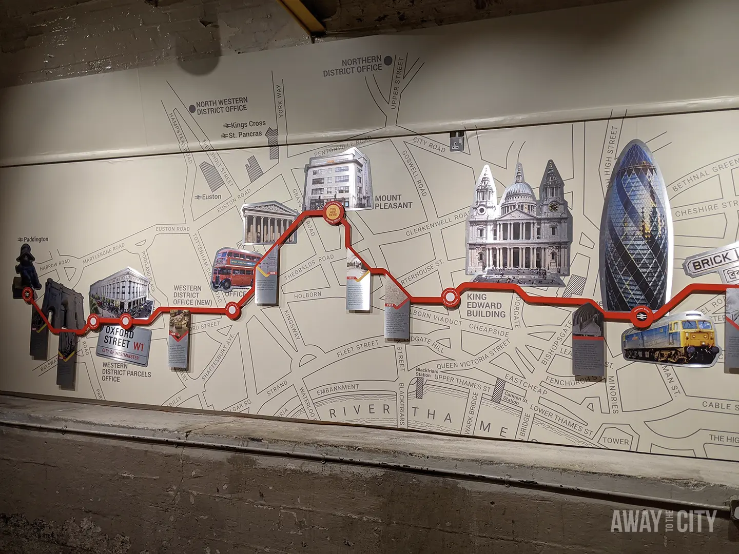 A map of London's mail rail route is displayed on a wall, with a red line connecting illustrated landmarks like Big Ben, a double-decker bus, and modern skyscrapers.