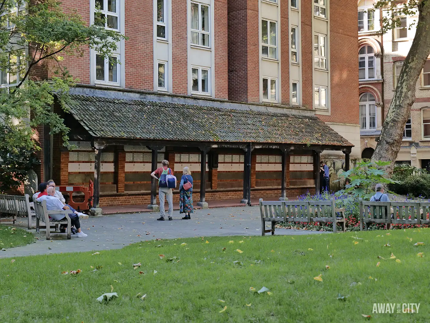 People relaxing and talking near the Memorial to Heroic Self-Sacrifice (covered area with plaques) in Postman's Park, London.