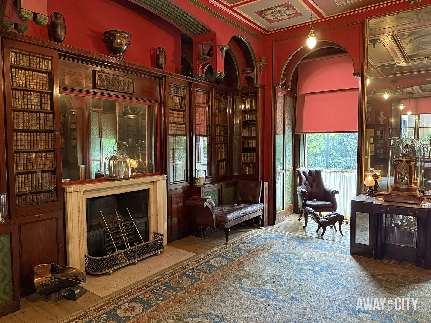 The interior of Sir John Soane's Museum features a study with a red colour scheme, numerous bookshelves, a fireplace, and a large leather chair