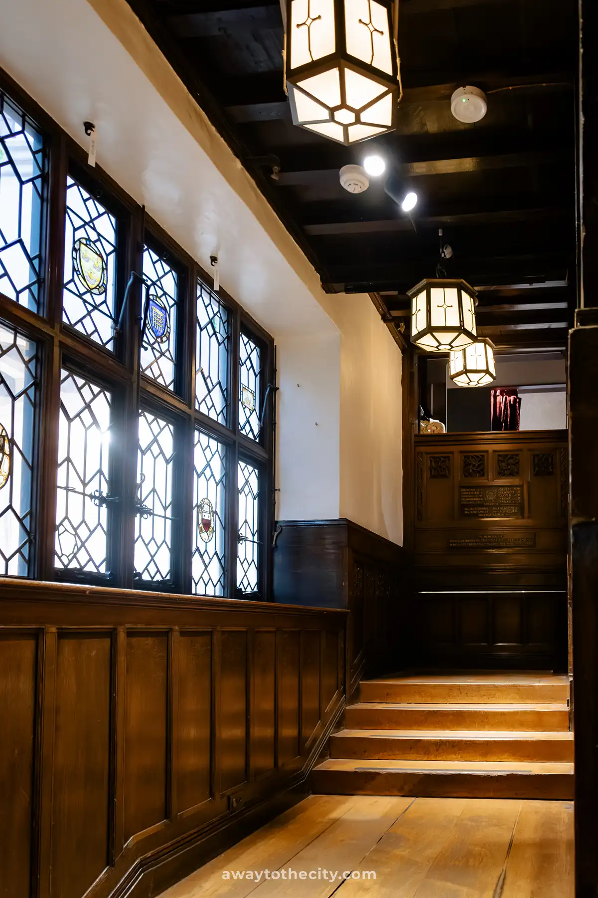 An old wooden staircase with patterned stained-glass windows is lit by hanging lanterns inside Liberty London.