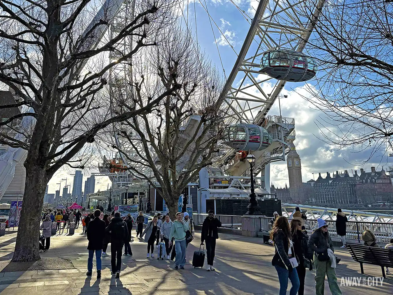 People walking along the South Bank in London with the London Eye and Big Ben in the background.