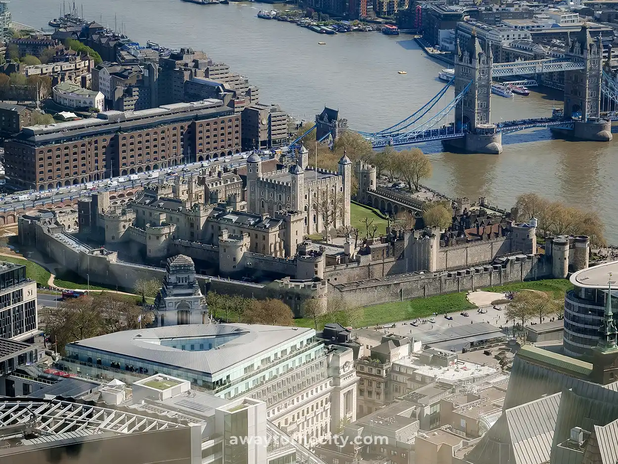 An aerial view of the Tower of London and Tower Bridge on the River Thames, surrounded by city buildings.