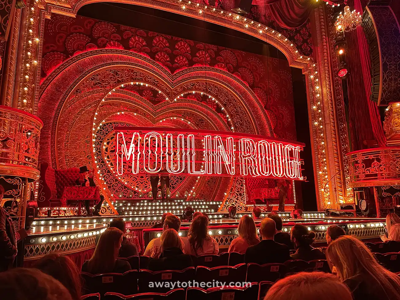 The Moulin Rouge theatre stage is dramatically lit in red, with a large glowing sign and ornate heart designs.